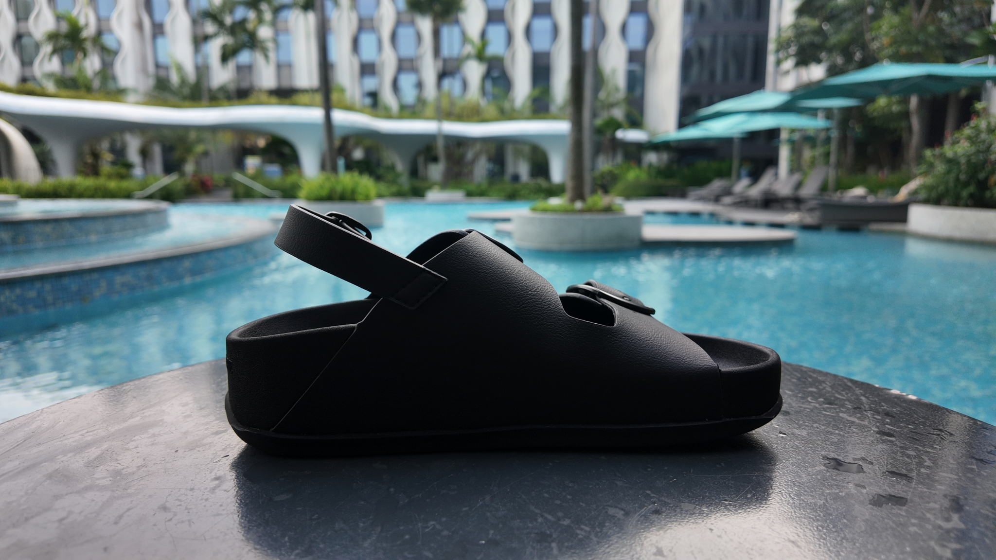 Black sandal on a table by a poolside with a blurred background