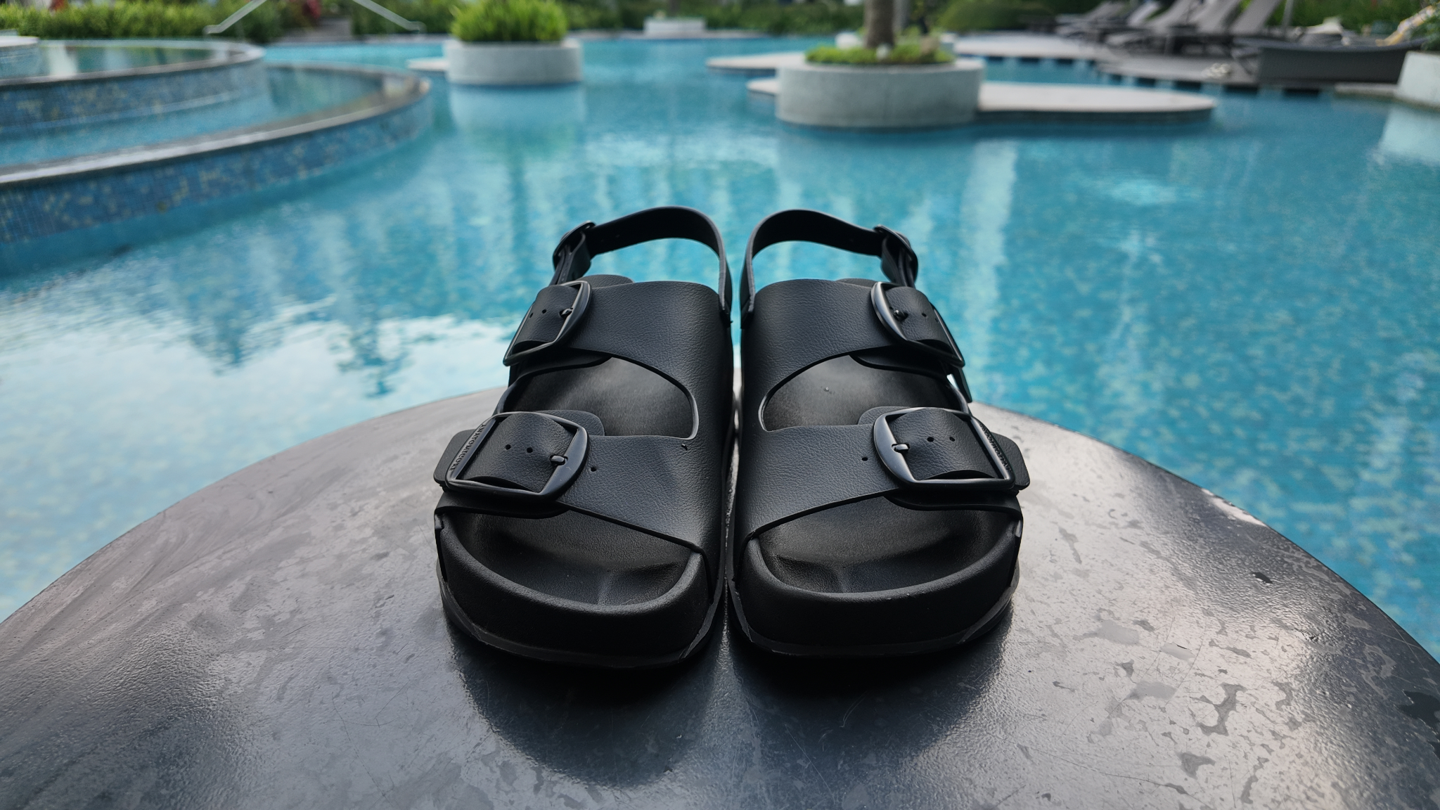 Black sandals on a stone ledge with a pool in the background