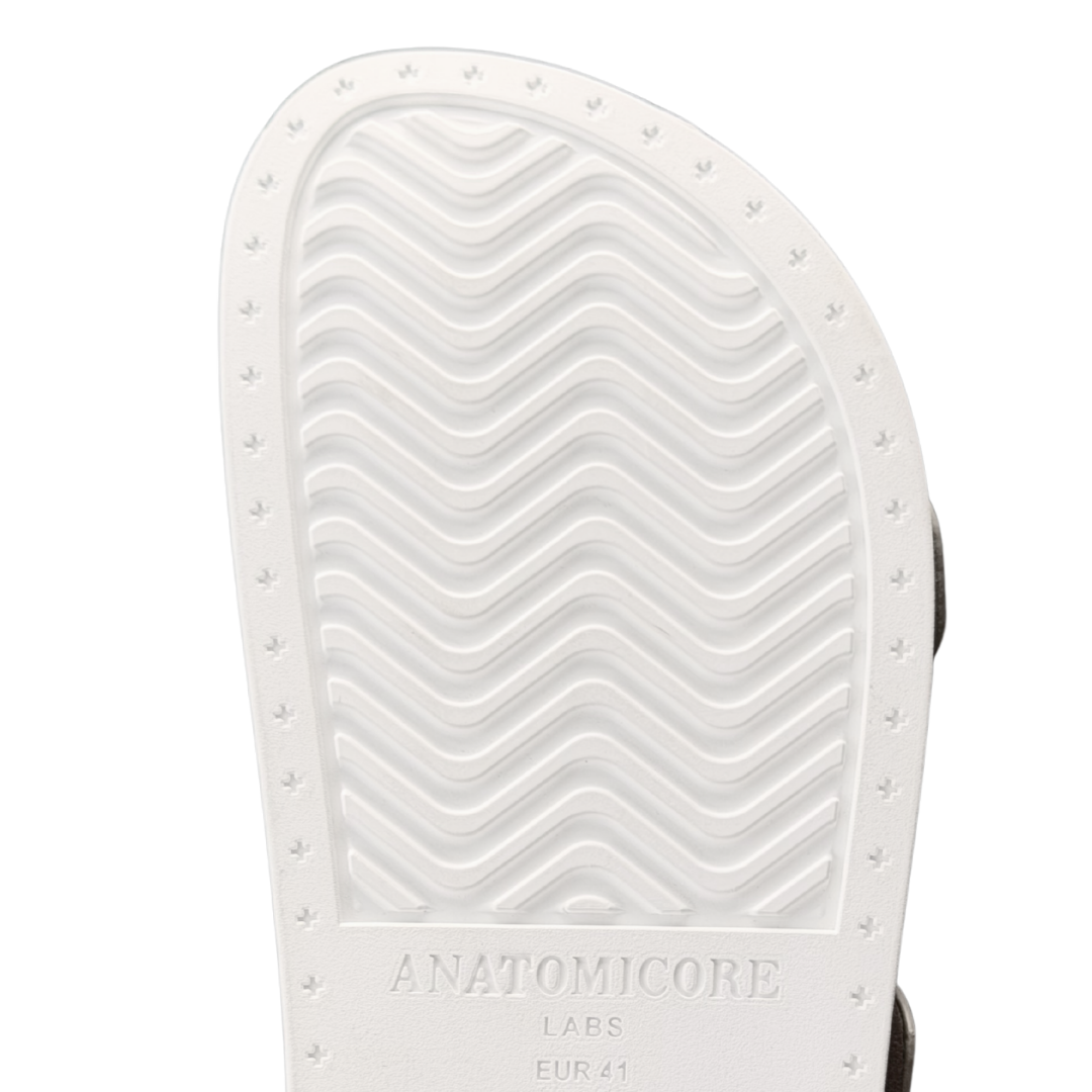 Close-up of the white textured outsole of a slide sandal, showing the wavy tread pattern and the embossed brand name 'ANATOMICORE LABS'.