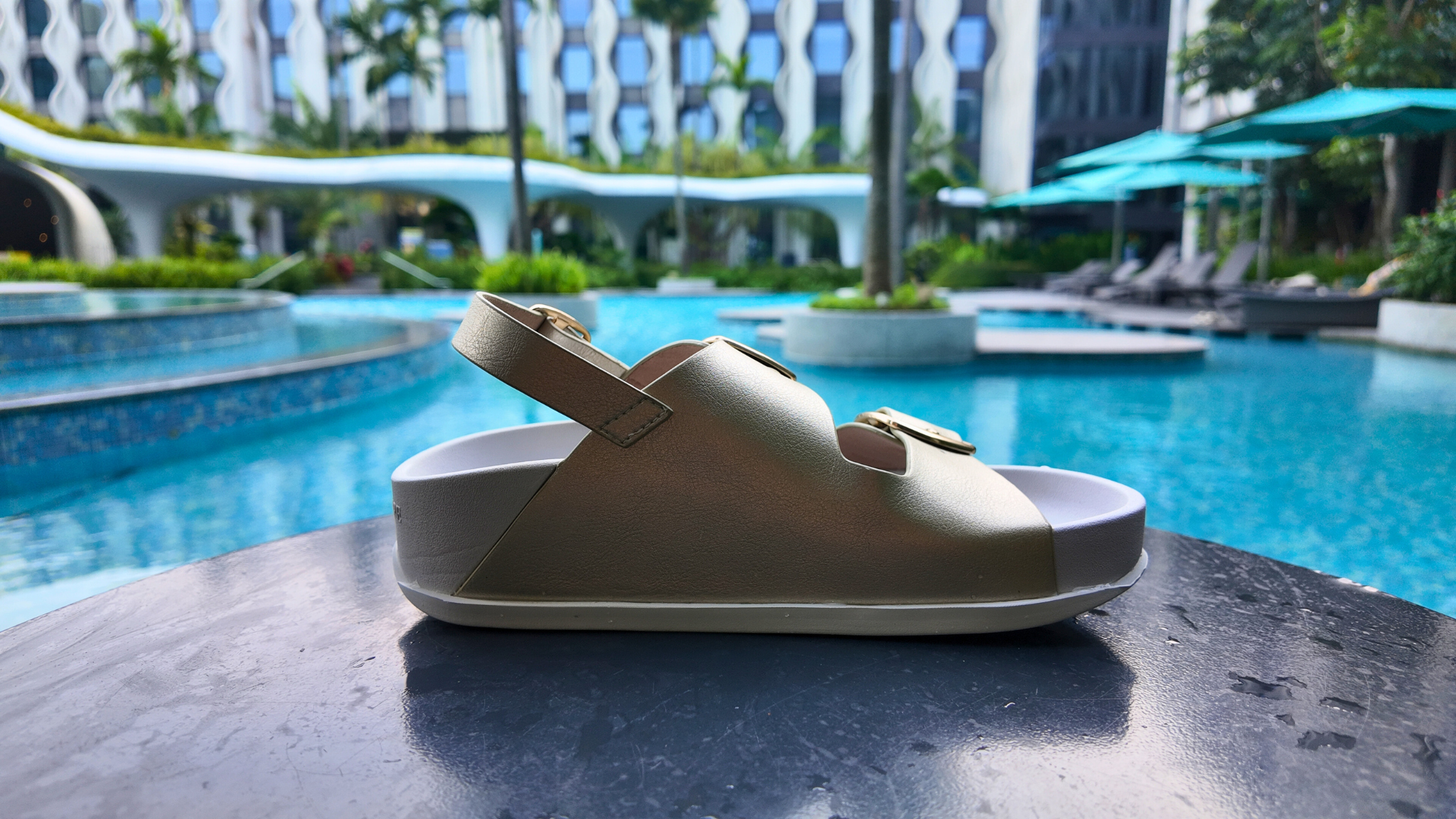 Gold sandal on a table by a poolside with a blurred background