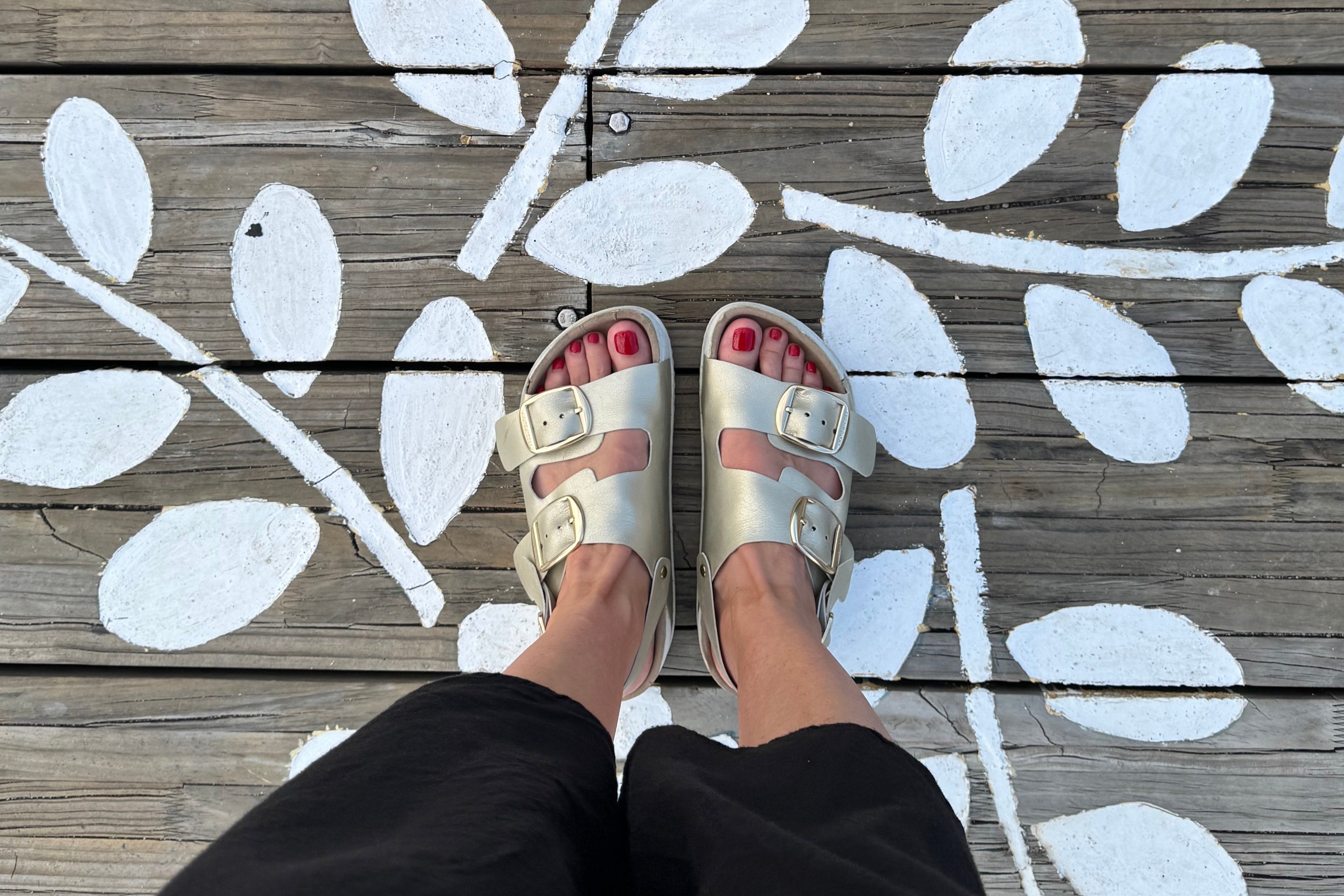 White leaf patterns on a wooden floor with feet wearing sandals stepping onto them.