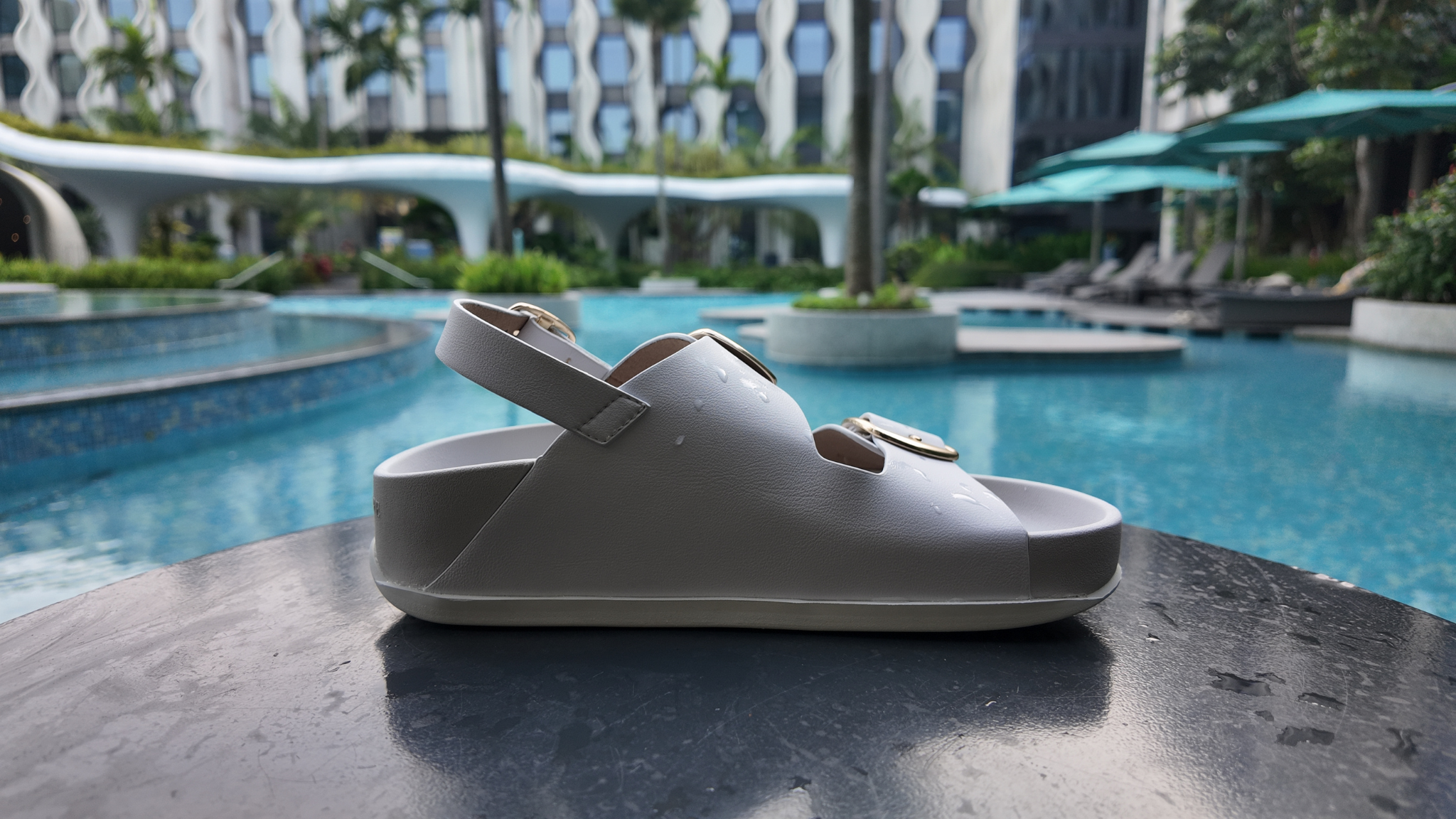 White sandal on a table with a pool and lounge chairs in the background