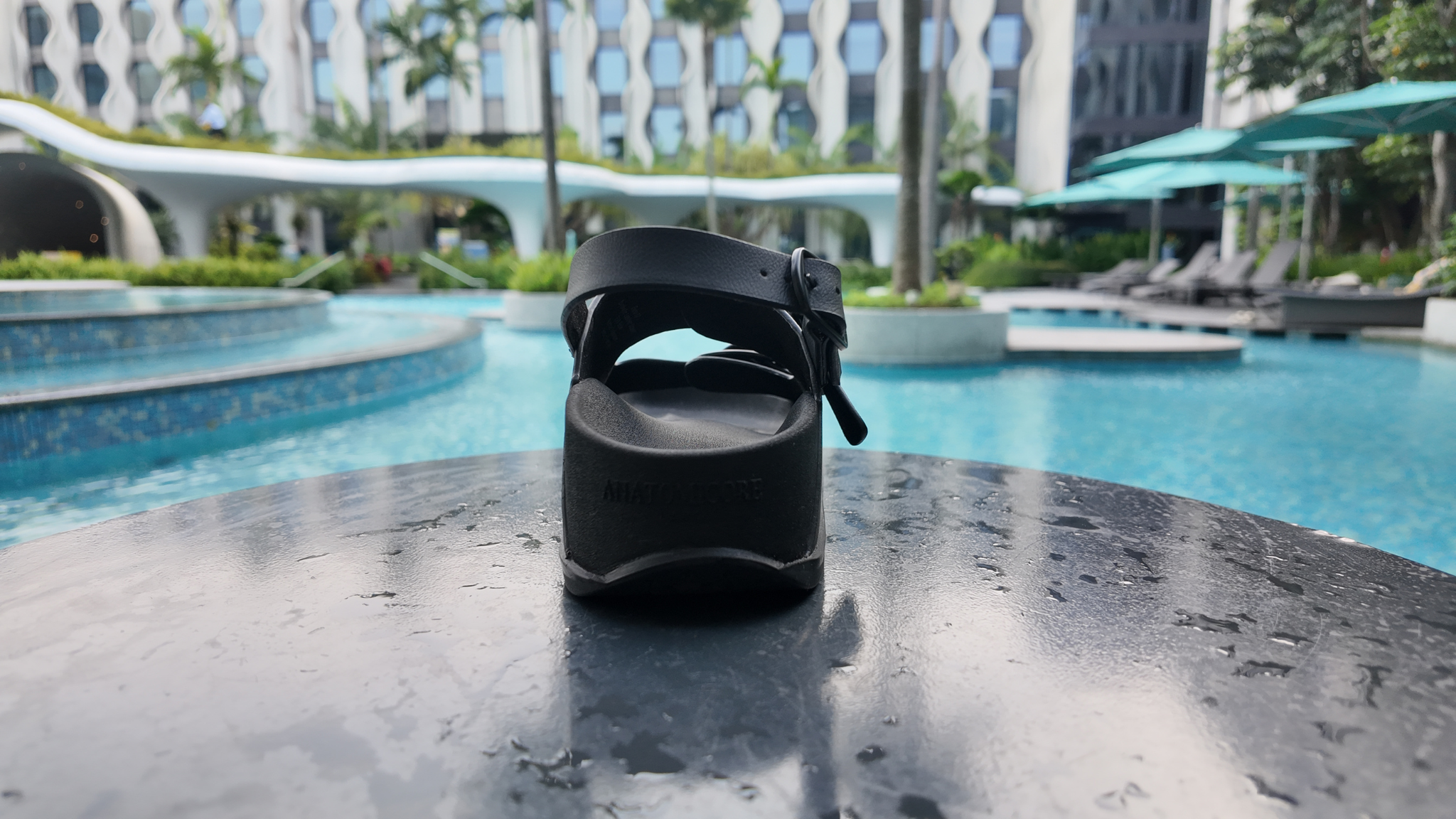 Black sandal on a table by a poolside with a building and umbrellas in the background