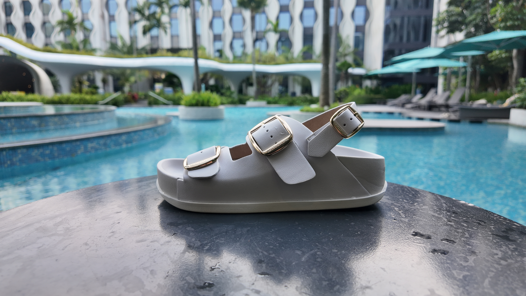 White sandal with gold buckles on a table by a poolside.